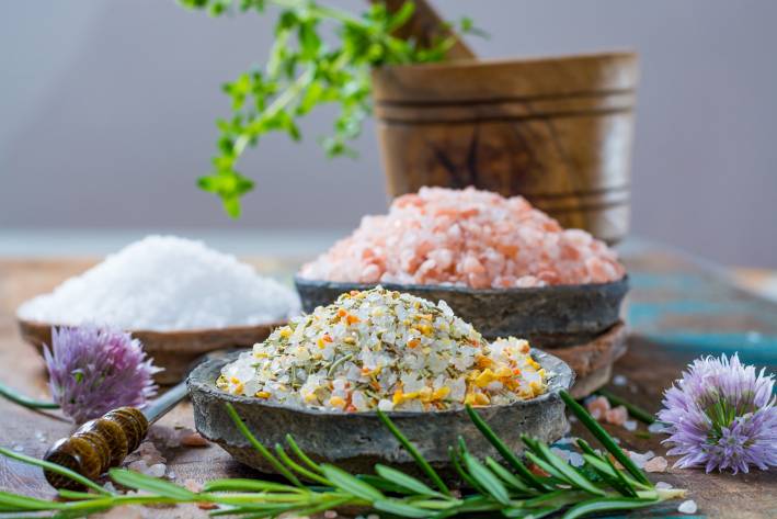 Different types of natural salt in stone bowls on wooden surface.