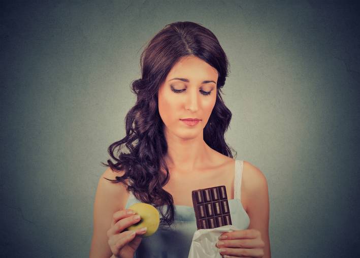 Woman with chocolate and apple trying to make a healthy choice.