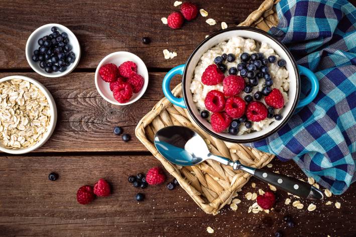 Oatmeal, oats and berries on a rustic wooden table.