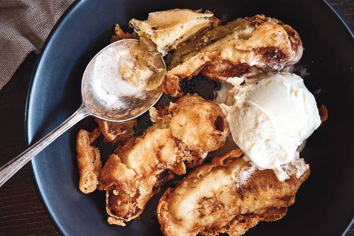 Banana fritters served in a blue bowl with vanilla ice cream.