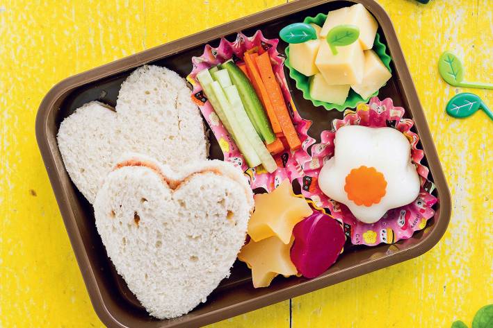 A bento box with heart-shaped sandwiches, homemade fruit snacks, cubed cheese and veggie sticks.