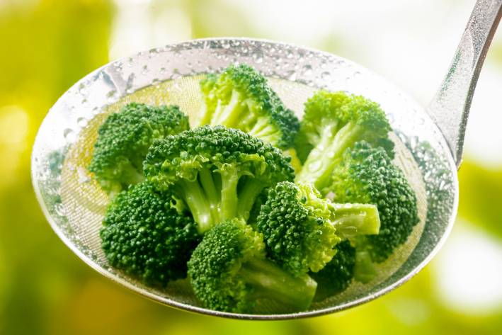 Steamed broccoli in a stainless steel ladle.