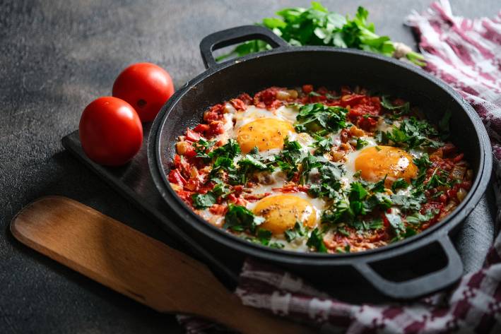 Baked Eggs with Tomatoes, Red Bell Pepper & Garlic in a iron pan on a dark background.