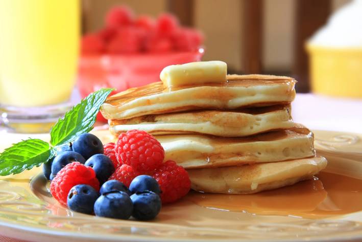 a stack of homemade pancakes from scratch with berries, syrup, and butter