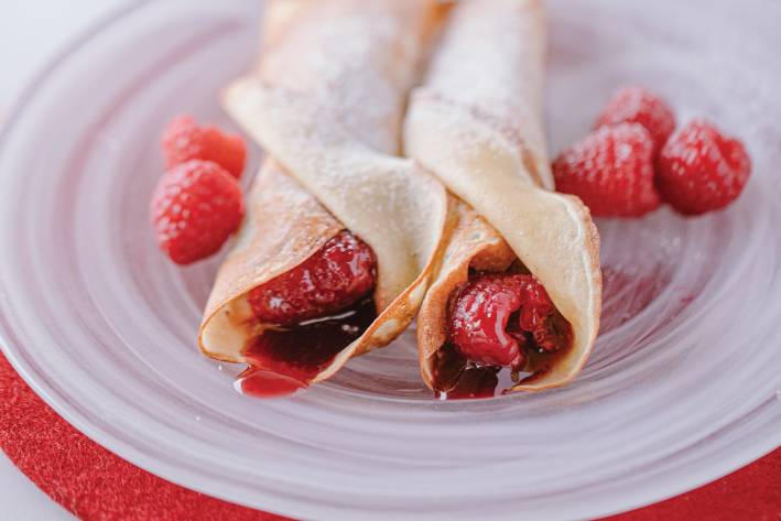 Jam Crêpes with Vanilla Sugar on a white swirled glass plate garnished with raspberries.
