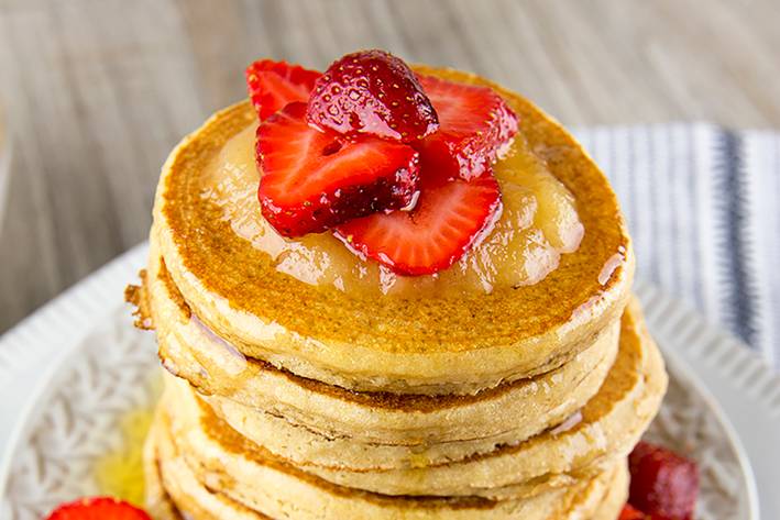 A steaming stack of pancakes with fruit on top