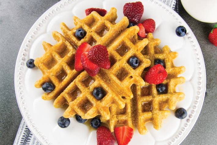 a plate of waffles with fruit and maple syrup