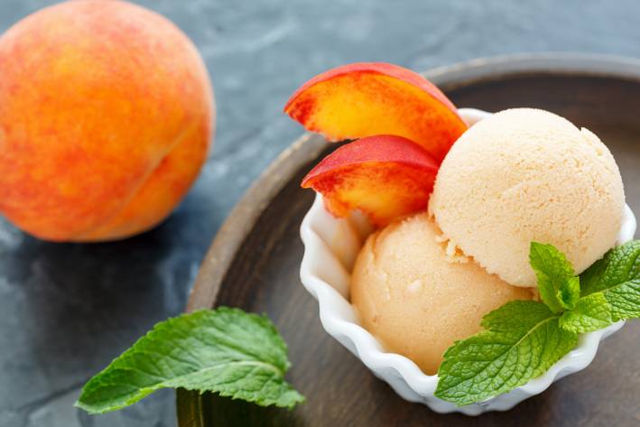 A scoop of coconut milk frozen dessert with peaches.