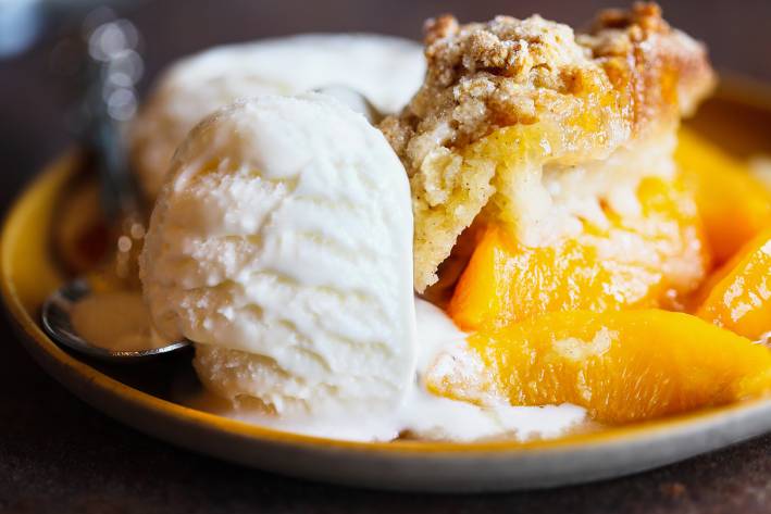 a bowl of warm peach cobbler and a scoop of vanilla ice cream