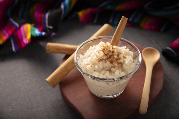 Mexican rice pudding in a glass cup beside a wooden spoon. 