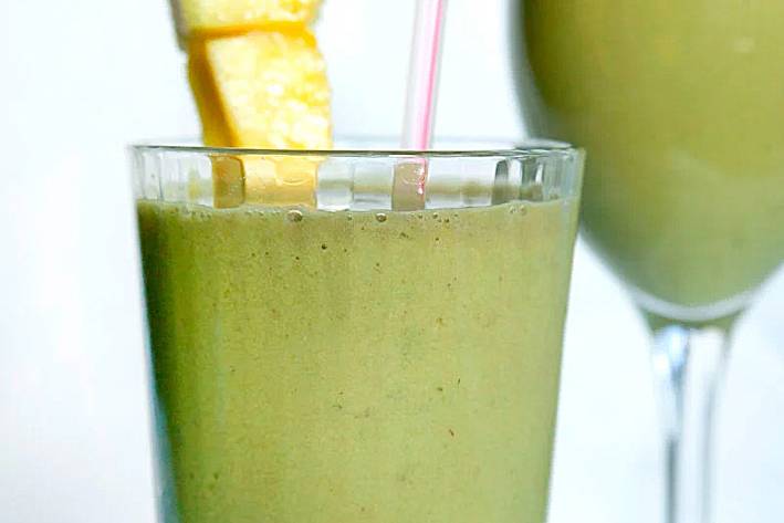 a glass of fruit smoothie with matcha garnished with pineapple