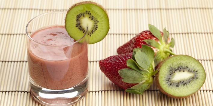 a glass of smoothie next to fresh strawberries and kiwi