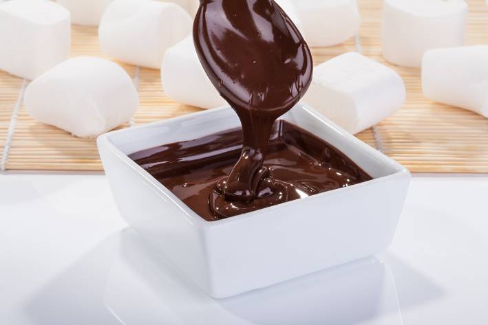 thick chocolate sauce drizzling from spoon to bowl