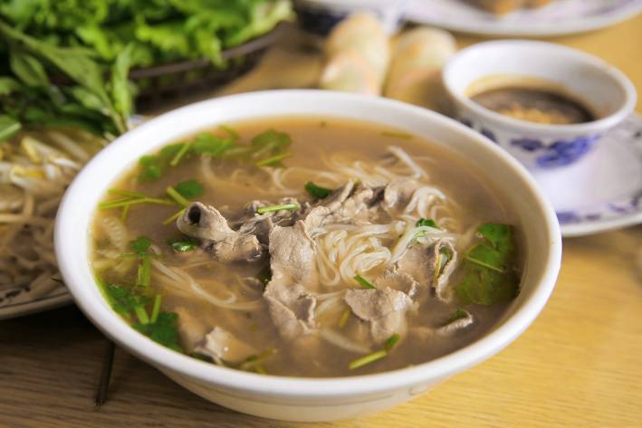 a bowl of soup with monkfish, noodles, and greens