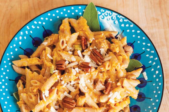 A bowl of penne with butternut squash and chicken sausage, garnished with sage