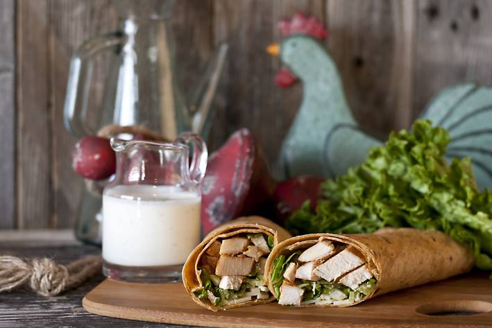 Chicken wrap with ranch dressing cut in half displayed on a cutting board. Farmhouse style background.