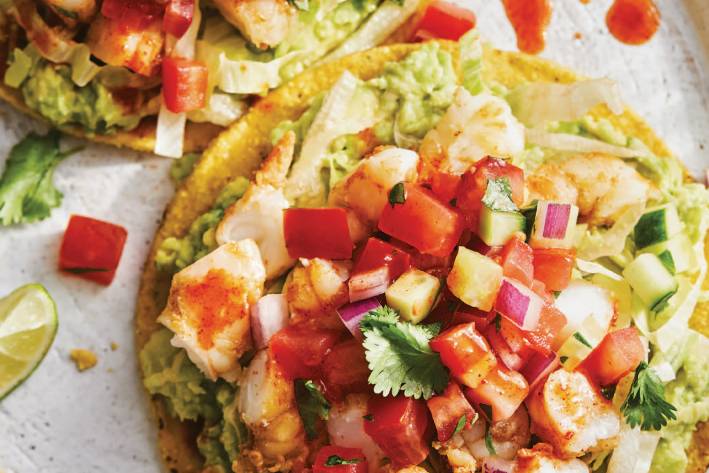 a tortilla slathered with guacamole and piled with shrimp and other toppings