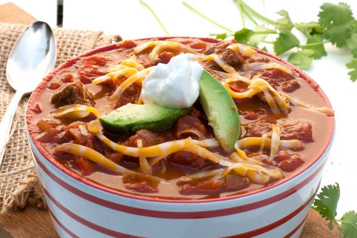 a bowl of chili con carne, topped with cheese, avocado, and sour cream