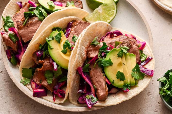 a plate of beefy steak tacos with slaw and avocado