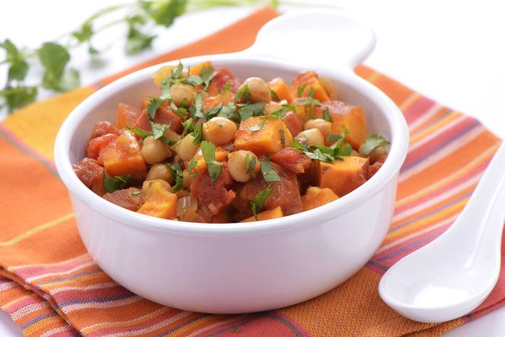 a bowl of curry full of sweet potatoes, chickpeas, and greens
