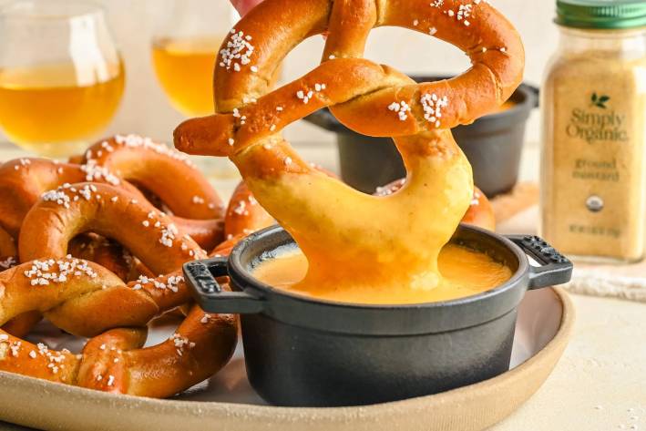 a soft pretzel being dipped in beer cheese