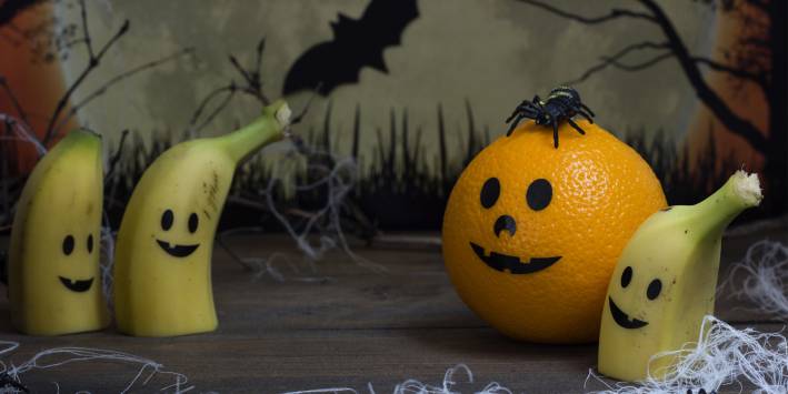 Bananas and an orange with jack-o-lantern smiles on them. Halloween backdrop.