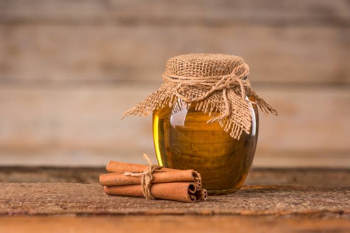 A jar of honey and cinnamon on a wooden background.