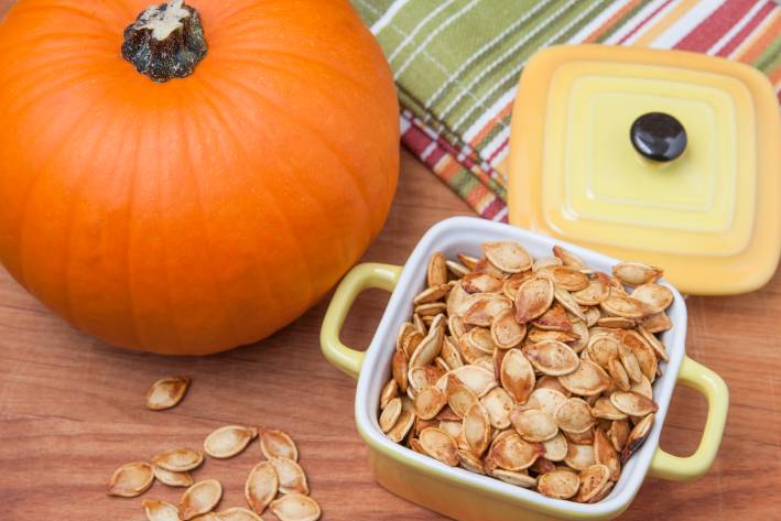 Roasted pumpkin seeds in a container next to a pumpkin. 