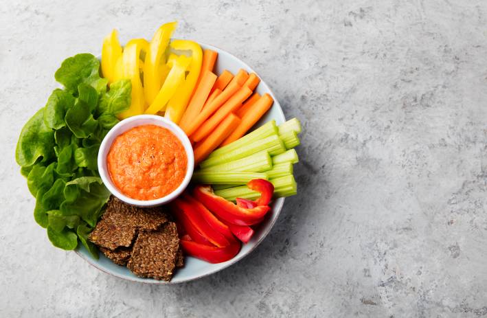 Assorted fresh vegetables with Roasted Red Pepper & Almond Dip. Stone background