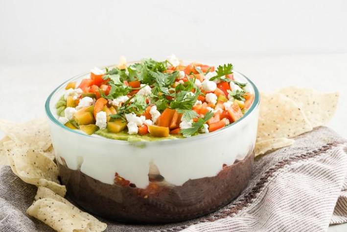 A bowl of seven-layer bean dip surrounded by tortilla chips