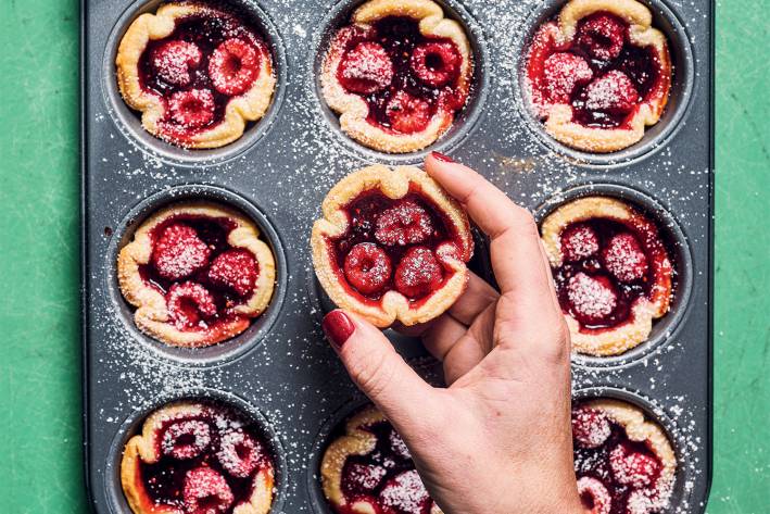 a woman removing raspberry tarts from a cupcake tin