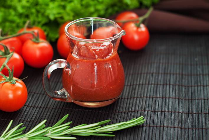 a pitcher of fresh ketchup surrounded by tomatoes