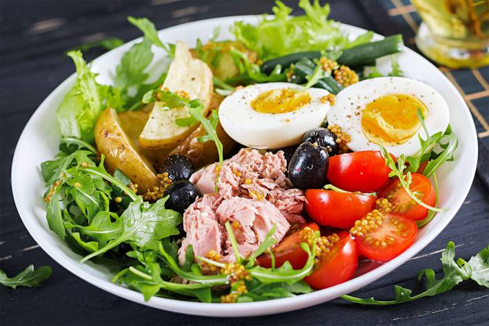 a salad of greens with eggs, cherry tomatoes, potatoes, and ham