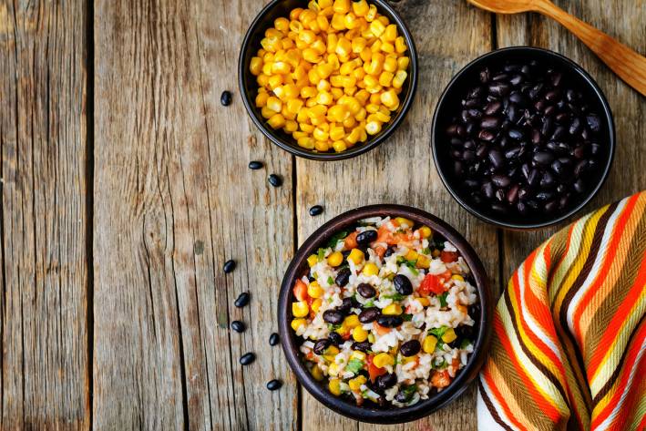 Fiesta salad, corn and black bean displayed in separate bowls. On a rustic farm table.