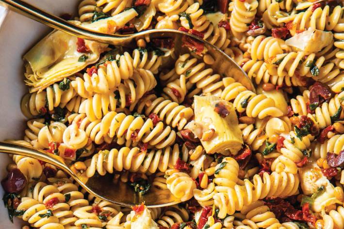 a bowl of fusilli with spinach, artichokes, and sun-dried tomatoes