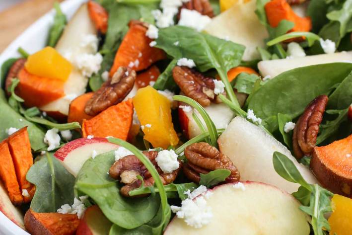 a salad with sweet potatoes, spinach, and nuts