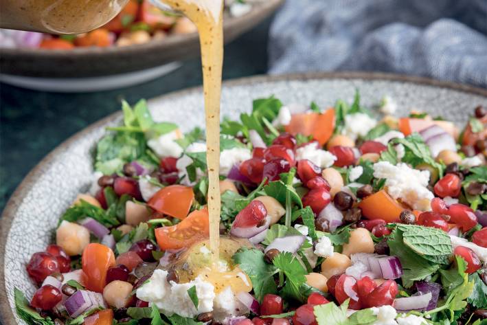 a bowl of lentils, vegetables, and herbs drizzled with dressing