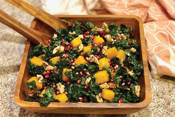 Kale, Butternut Squash, & Pomegranate Salad in a wooden salad bowl with wooden salad utensils.