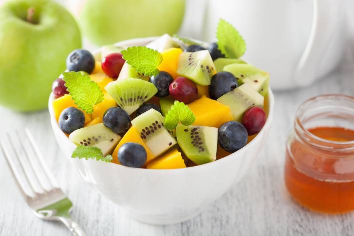 a bowl of kiwi, melon, blueberries, and grapes, with a honey sauce