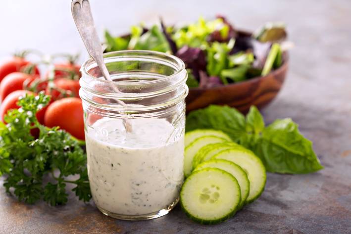 a mason jar of homemade ranch dressing, plus salad greens and veggies for dipping