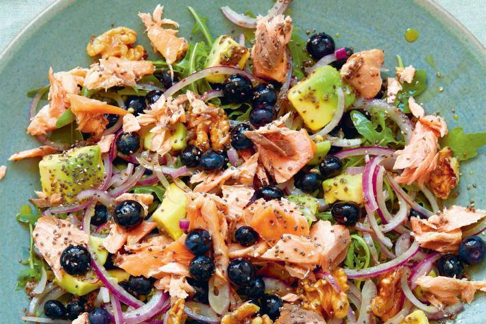 a plate with smoked salmon, blueberries, nuts, and greens