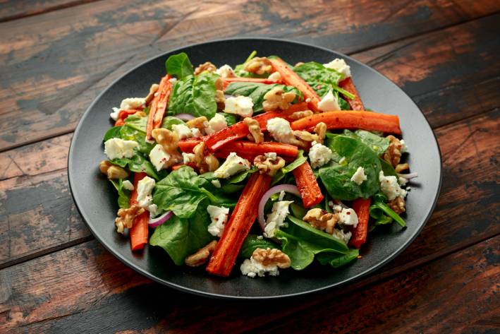 Spinach and Roasted Carrot Salad Grey salad plate filled with spinach, roasted carrots, cheese, and walnuts.