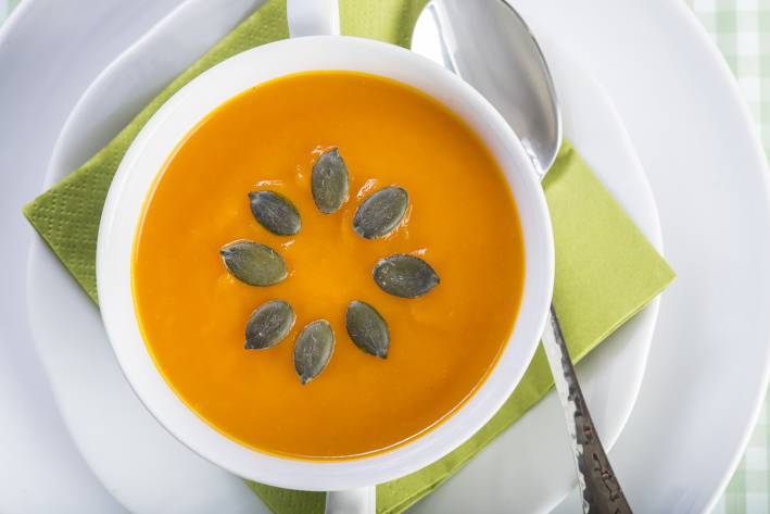 Creamy pumpkin soup, in a white bowl, decorated with seeds in a sunburst pattern.