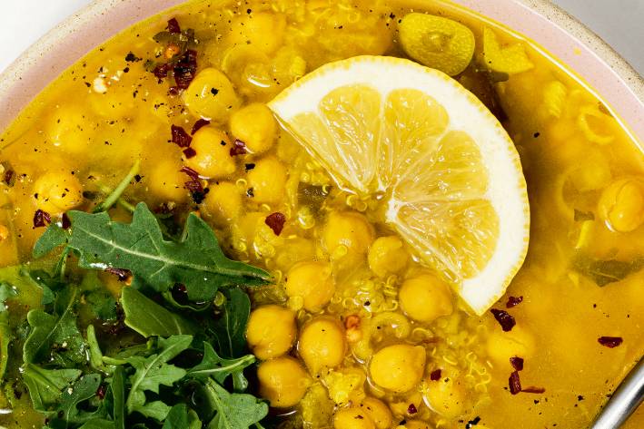 a bowl of chickpea soup garnished with arugula and lemon