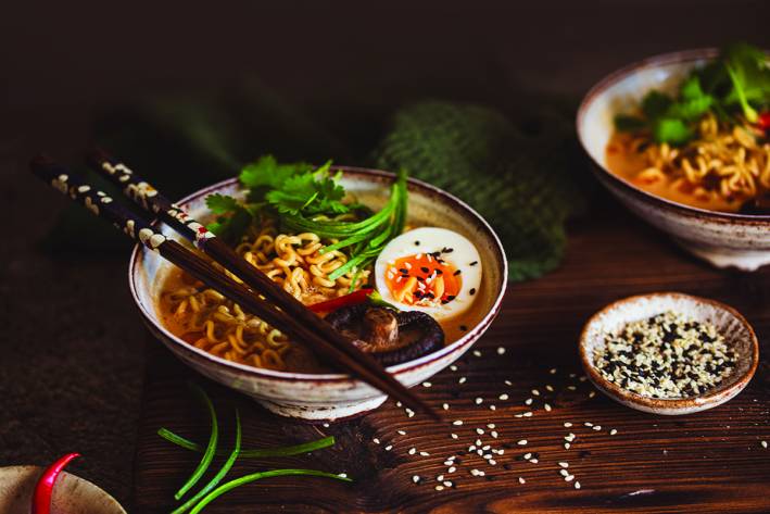 Ramen Noodles with Shiitake Mushrooms A bowl of ramen noodles with half a hard-boiled egg and cilantro in a small white bowl with brown chopsticks resting on top.