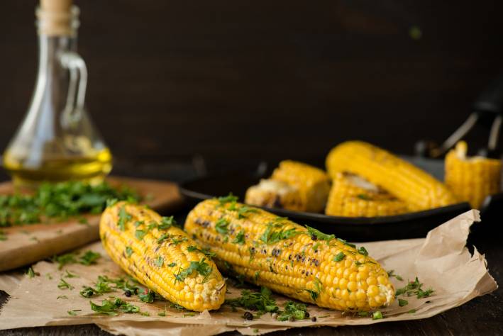 Grilled Lime & Cilantro Corn on the Cob on parchment paper with corn, oil and cilantro in the background.