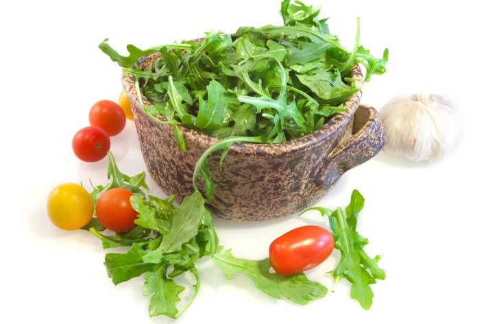 Bowl of arugula with cherry tomatoes and a bulb of garlic surrounding the bowl