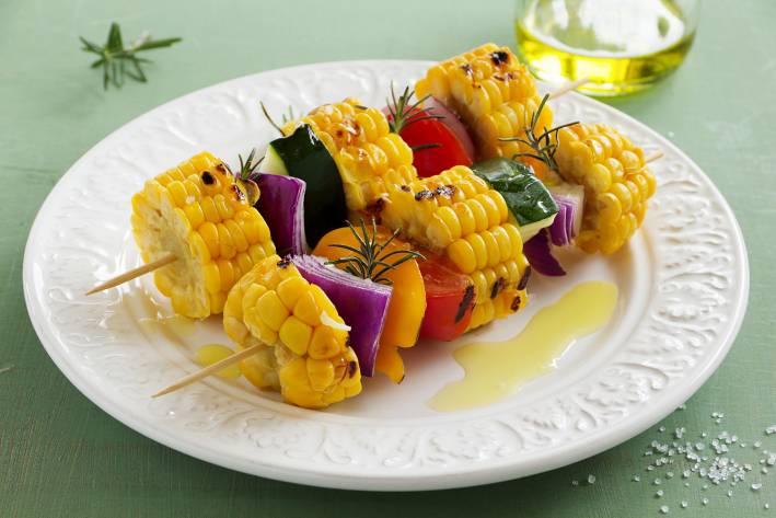a plate of grilled vegetables on skewers with oil and seasoning
