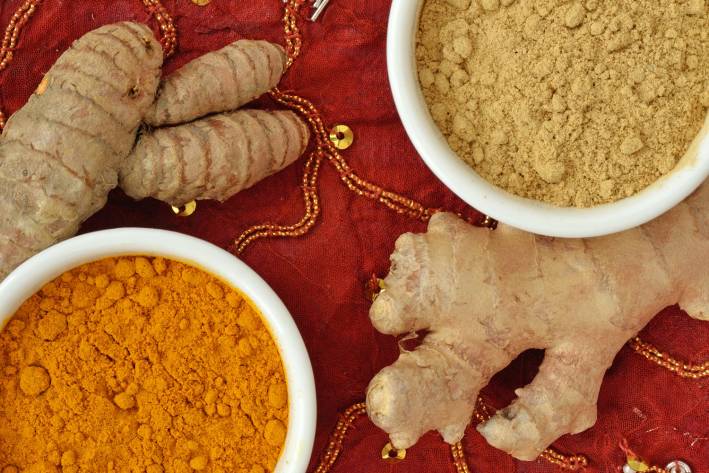 Powder and roots of turmeric and ginger on indian carpet background