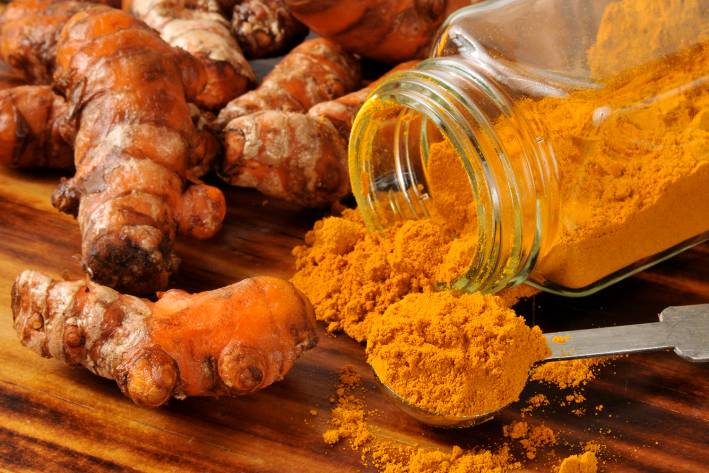 A jar of ground turmeric next to fresh roots.